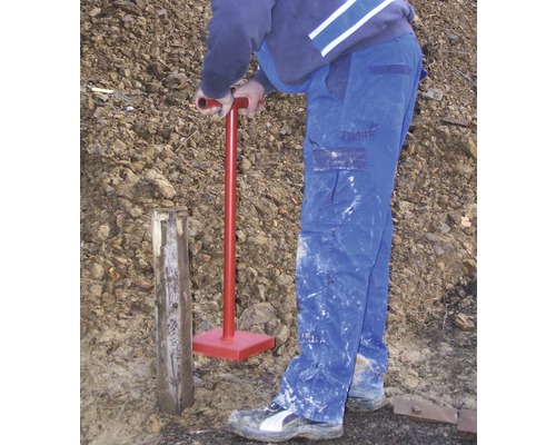 Een persoon slaat met een grondstamper een houten paal in de grond.