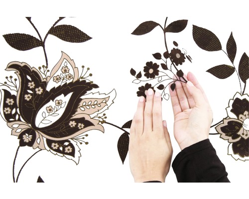 Persoon brengt een bruine, zelfklevende rand met bloemmotief aan op een witte muur