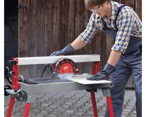 Een man met veiligheidsbril en handschoenen bedient een tegelsnijmachine om een tegel te snijden.