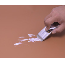 Een hand gebruikt een glasschraper om verf van een oppervlak te verwijderen.