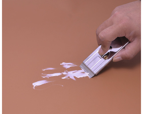 Een hand gebruikt een glasschraper om verf van een oppervlak te verwijderen.