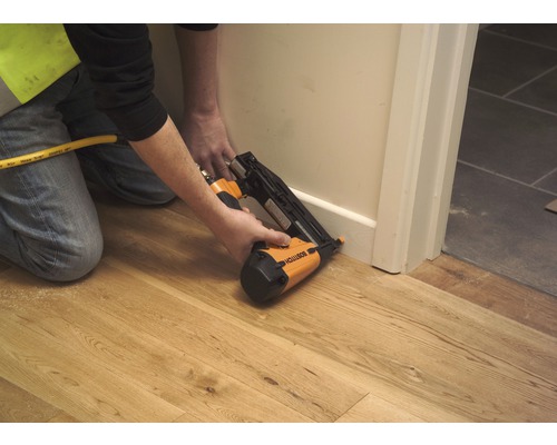 Een persoon bevestigt een plint aan een muur met een pneumatische tacker.