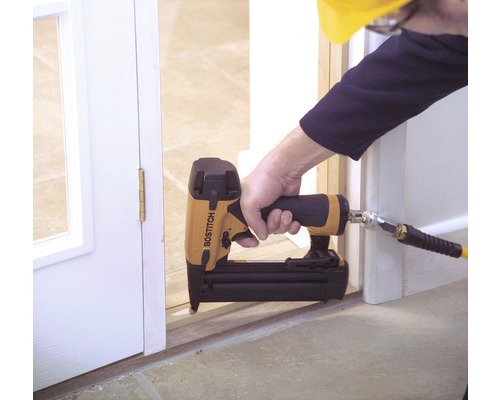 Iemand gebruikt een Bostitch tacker om een deurkozijn te bevestigen.