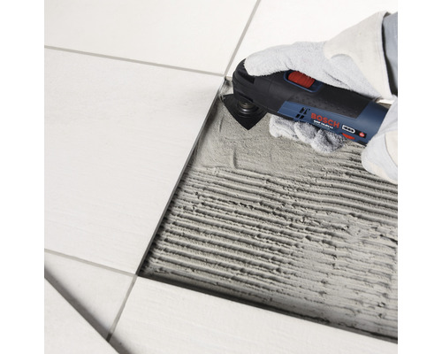 Een persoon verwijdert een tegel met een multifunctioneel gereedschap.