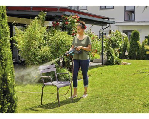 Vrouw reinigt tuinstoel met hogedrukreiniger in de tuin.
