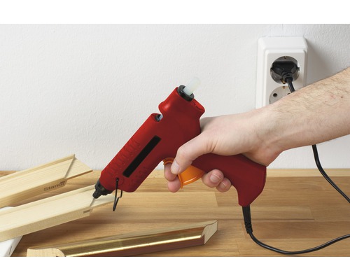 Een hand houdt een lijmpistool vast om een houten frame aan elkaar te lijmen.