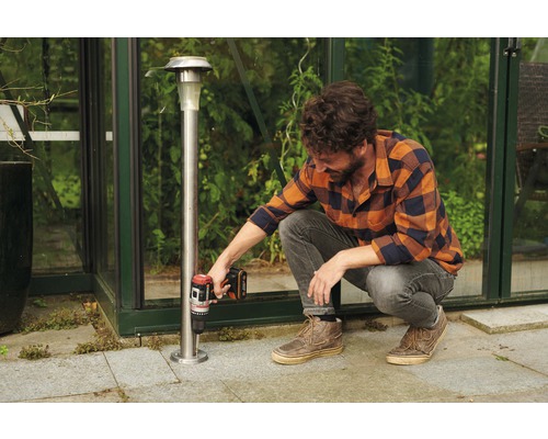 Een man bevestigt een solarlamp met een accuboormachine in de tuin.