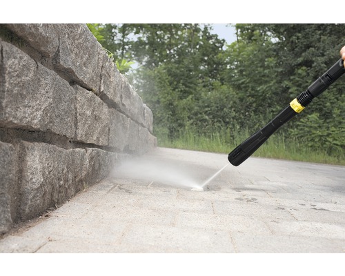 Hogedrukreiniger in gebruik voor het reinigen van een stenen muur en een voetpad
