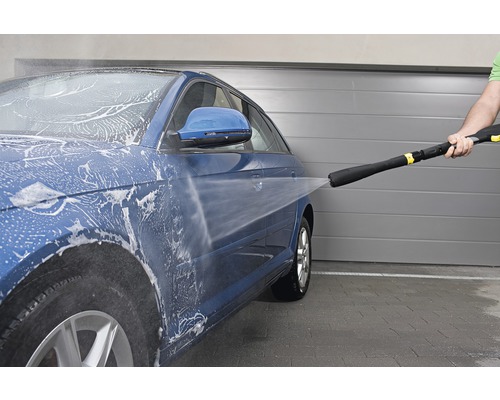 Een man maakt een blauwe auto schoon met een hogedrukreiniger.