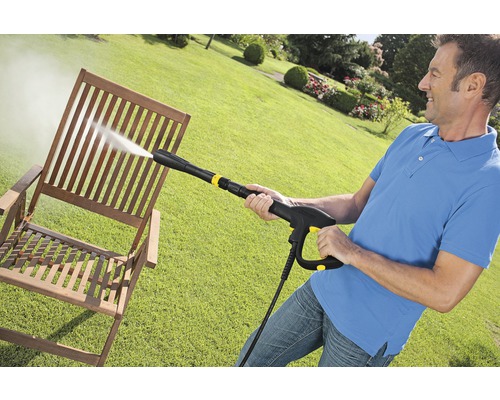 Man reinigt een houten stoel met een hogedrukreiniger in de tuin.