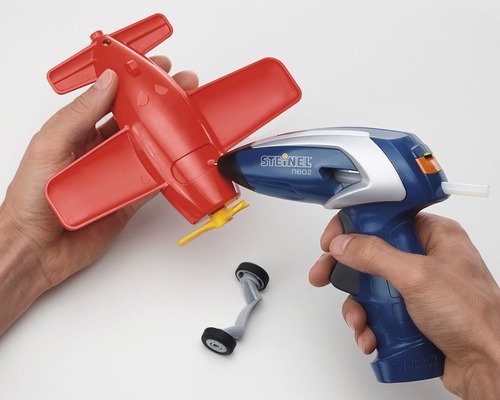 Persoon lijmt een rood speelgoedvliegtuig in elkaar met een lijmpistool