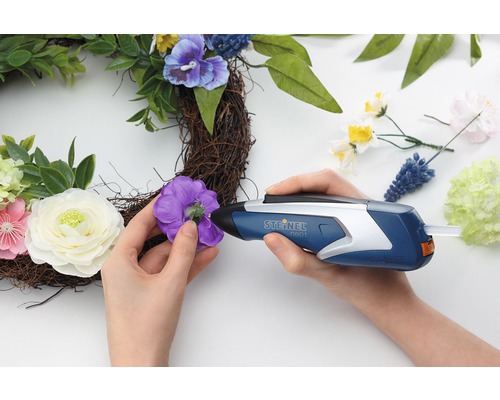 Persoon bevestigt met een lijmpistool een bloem aan een krans.