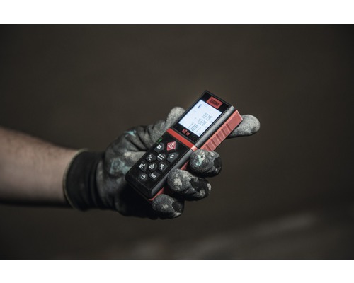 Een hand met een werkhandschoen houdt een afstandsmeter vast