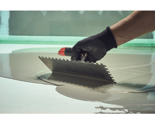 Vakman spreidt egalisatiemortel uit met een vlakspaan