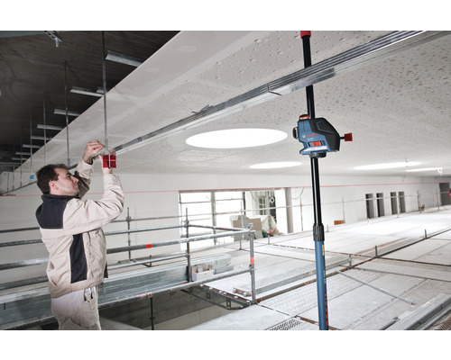 Een man monteert een plafondconstructie met een kruislijnlaser en een plafondstatief in een ruimte.