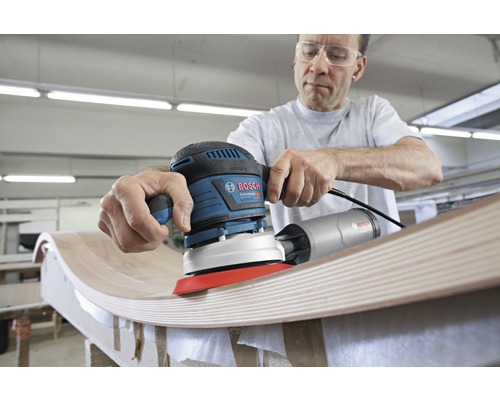 Een man schuurt hout met een Bosch excentrische schuurmachine.