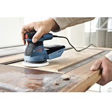 Een man gebruikt een Bosch excentrische schuurmachine om een houten deur te schuren.