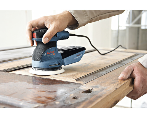 Een man gebruikt een Bosch excentrische schuurmachine om een houten deur te schuren.