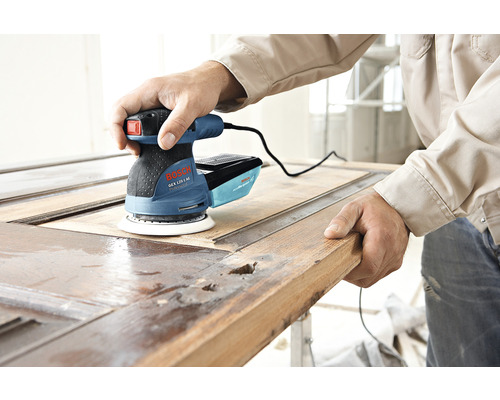 Een man gebruikt een Bosch excentrische schuurmachine om een houten deur te schuren.