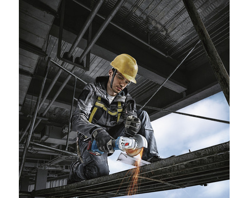 Een bouwvakker met een veiligheidshelm gebruikt een haakse slijper op een steiger.