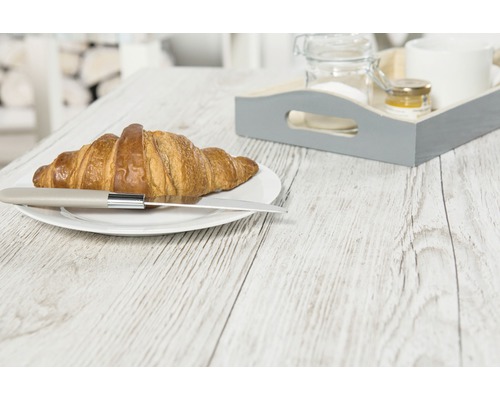 Een croissant met een mes op een bord en een ontbijtblad op een houten tafel.