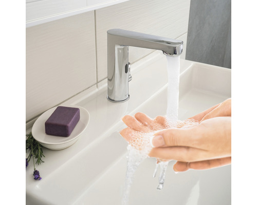 Persoon wast handen onder een verchroomde kraan in de wastafel.