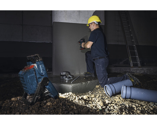 Ambachtsman aan het werk met boormachine, bouwlamp en afvoerpijpen op een bouwplaats