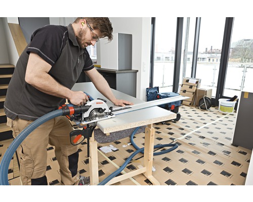 Ambachtsman zaagt met een cirkelzaag een werkstuk op een werkbank. Een afzuigslang is aan de zaag bevestigd.