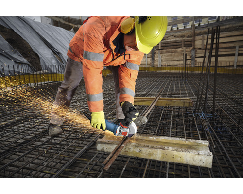 Een bouwvakker gebruikt een haakse slijper om stalen staven te snijden op een bouwplaats.