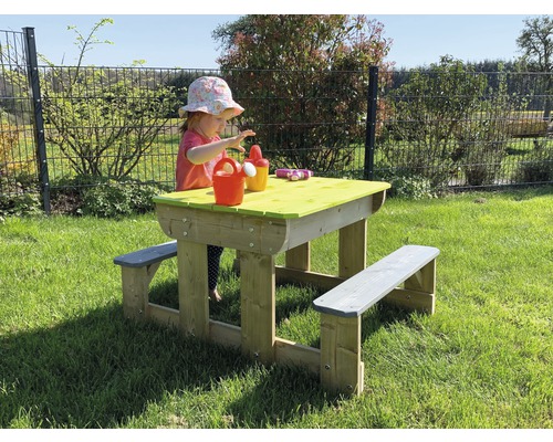 Kind speelt aan picknicktafel in de tuin. De houten tafel heeft banken en een groen tafelblad.