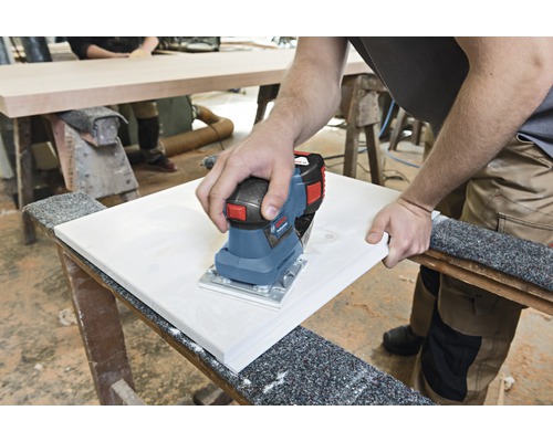 Een persoon schuurt een werkstuk met een elektrische schuurmachine.