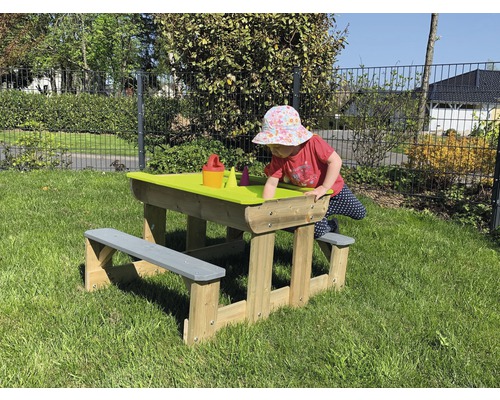 Kind speelt aan zandtafel met houten bank in de tuin