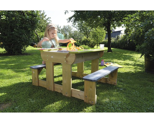 Kind speelt aan houten picknicktafel met zandbakfunctie in de tuin.
