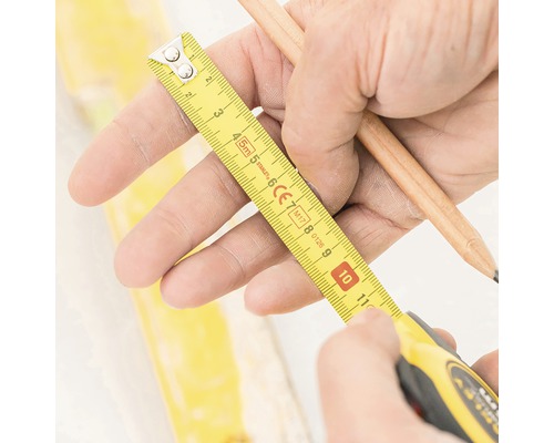 Handen houden een gele rolmaat en een potlood vast om te meten.