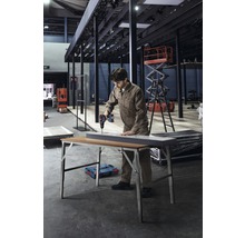 Een man boort met een accuboormachine een werkstuk op een werktafel in een werkplaats.