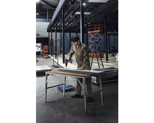 Een man boort met een accuboormachine een werkstuk op een werktafel in een werkplaats.