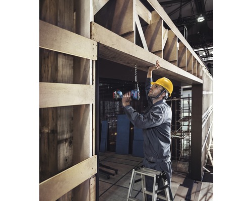 Een vakman boort met een boormachine in een houten frame op een bouwplaats.