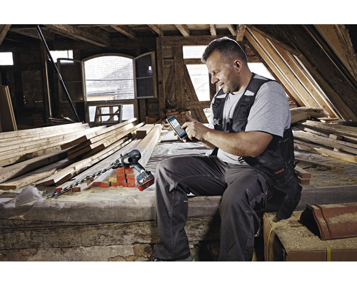 Man met smartphone en accuboormachine op zolder met houten balken