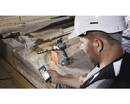 Ambachtsman met smartphone naast een accuboormachine op een bouwplaats