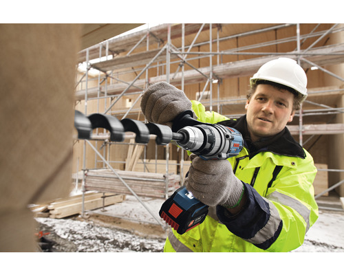 Een bouwvakker boort een gat in een stuk hout met een accuschroefboormachine.