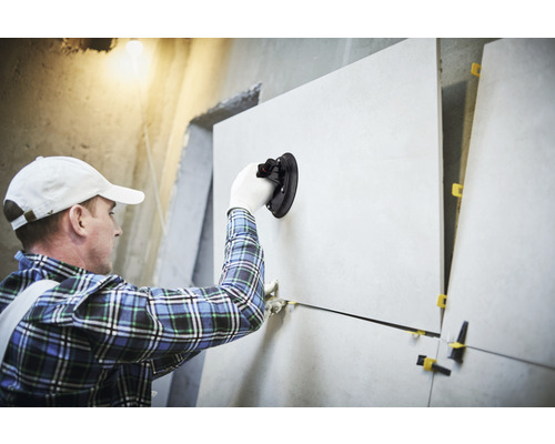 Tegelzetter met zuignapgereedschap legt tegels op een muur