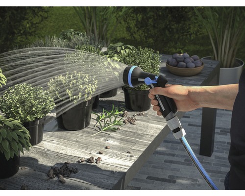 Hand besproeit planten met een tuinspuit op een tafel buiten.