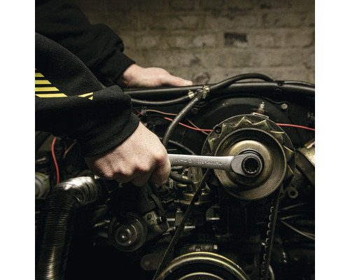 Een persoon gebruikt een moersleutel op een automotor.