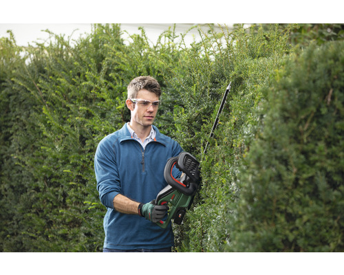 Man snoeit heg met accu heggenschaar in de tuin.