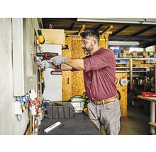 Ambachtsman boort met een accuboormachine een gat in een muur in een werkplaats.