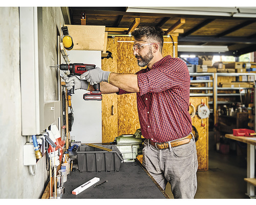 Ambachtsman boort met een accuboormachine een gat in een muur in een werkplaats.