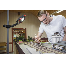 Man werkt aan een modelspoorbaan onder een werklamp.