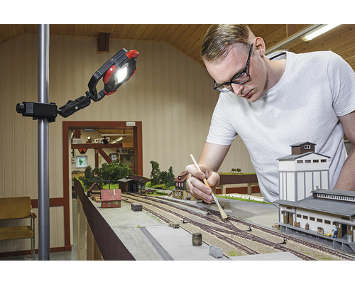 Man werkt aan een modelspoorbaan onder een werklamp.