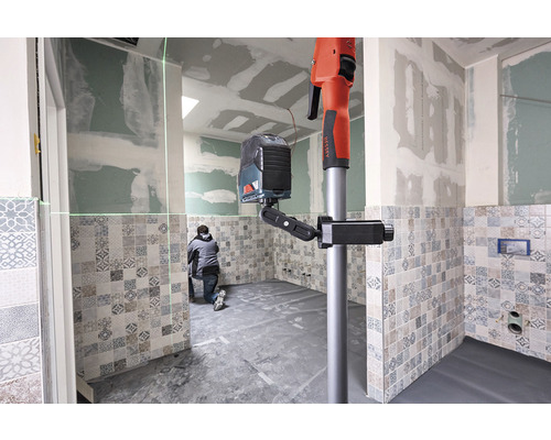 Een vakman gebruikt een lijnlaser nivelleerinstrument met statief in een betegelde badkamer.