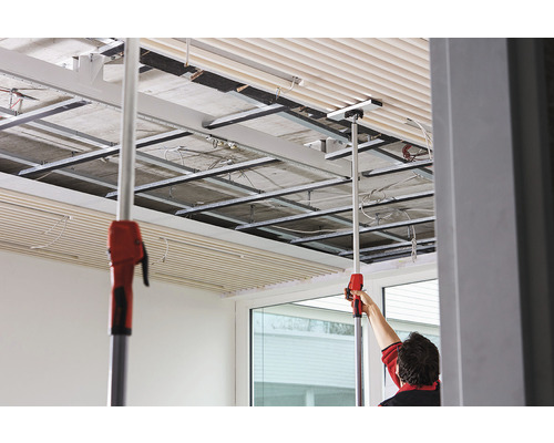 Montage van plafondplaten met montagegereedschap in een ruimte met plafondconstructie.